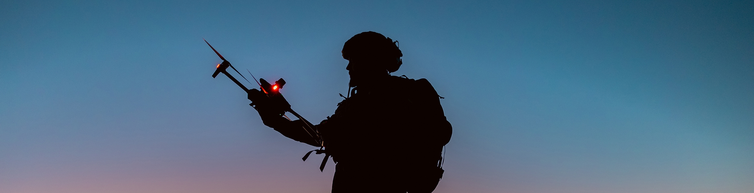 Silhouettes of soldiers are using drone for scouting during military operation against the backdrop of a sunset. Application of modern technology during war